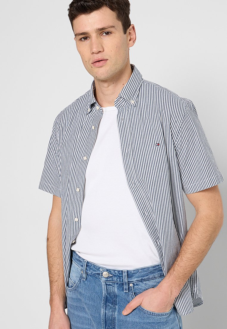 Chemise à manches courtes rayée en bleu marine et blanc avec un col boutonné et un petit logo, associée à un jean bleu clair.