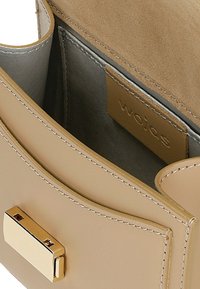 Beige leren handtas met een gladde textuur, voorzien van een gouden sluiting en subtiele stiksels. Inclusief grijze voering en een merklabel aan de binnenkant.