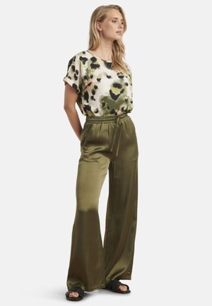 Satijnen groene broek met wijde pijpen en een elastische tailleband, gecombineerd met een kortemouwen top met een veelkleurig luipaardprint patroon.