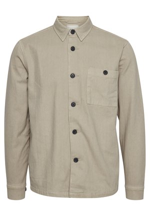 Chemise boutonnée beige en tissu durable, dotée d'un col pointu, de boutons noirs et d'une poche poitrine unique. Texture lisse, manches longues.