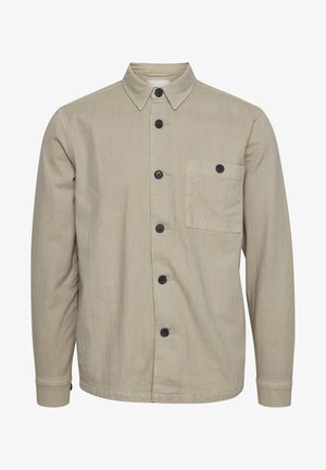 Chemise boutonnée beige en tissu durable, dotée d'un col pointu, de boutons noirs et d'une poche poitrine unique. Texture lisse, manches longues.