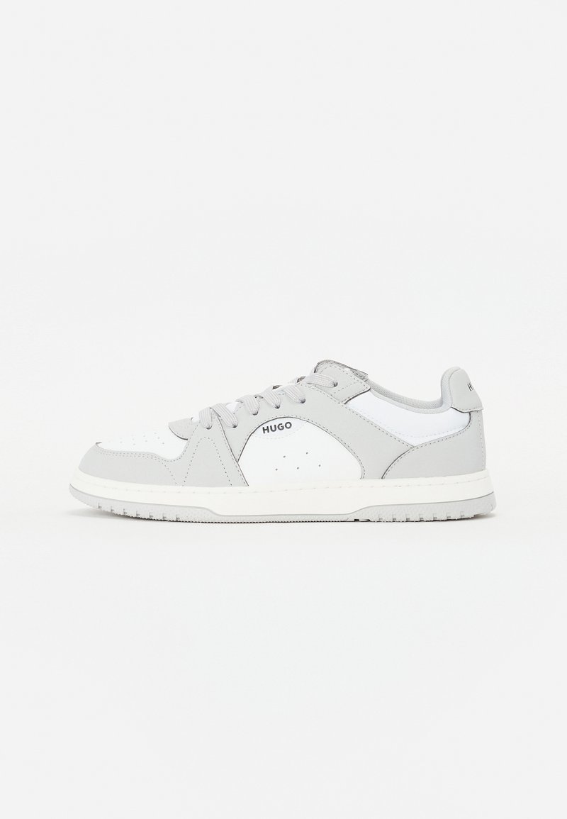 Sneaker grigio e bianco con finitura in pelle liscia, dettagli perforati e suola in gomma. Presenta un logo sul lato e design con lacci.