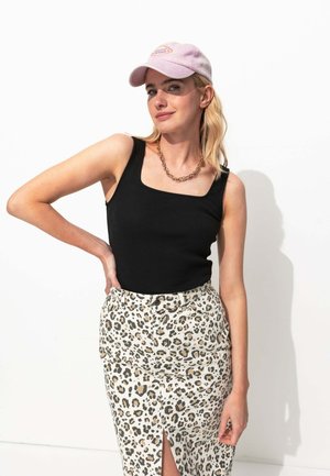 Débardeur noir à côtes porté avec une jupe léopard à fente haute. Une casquette de baseball rose pâle et un collier à chaîne épaisse complètent le look.