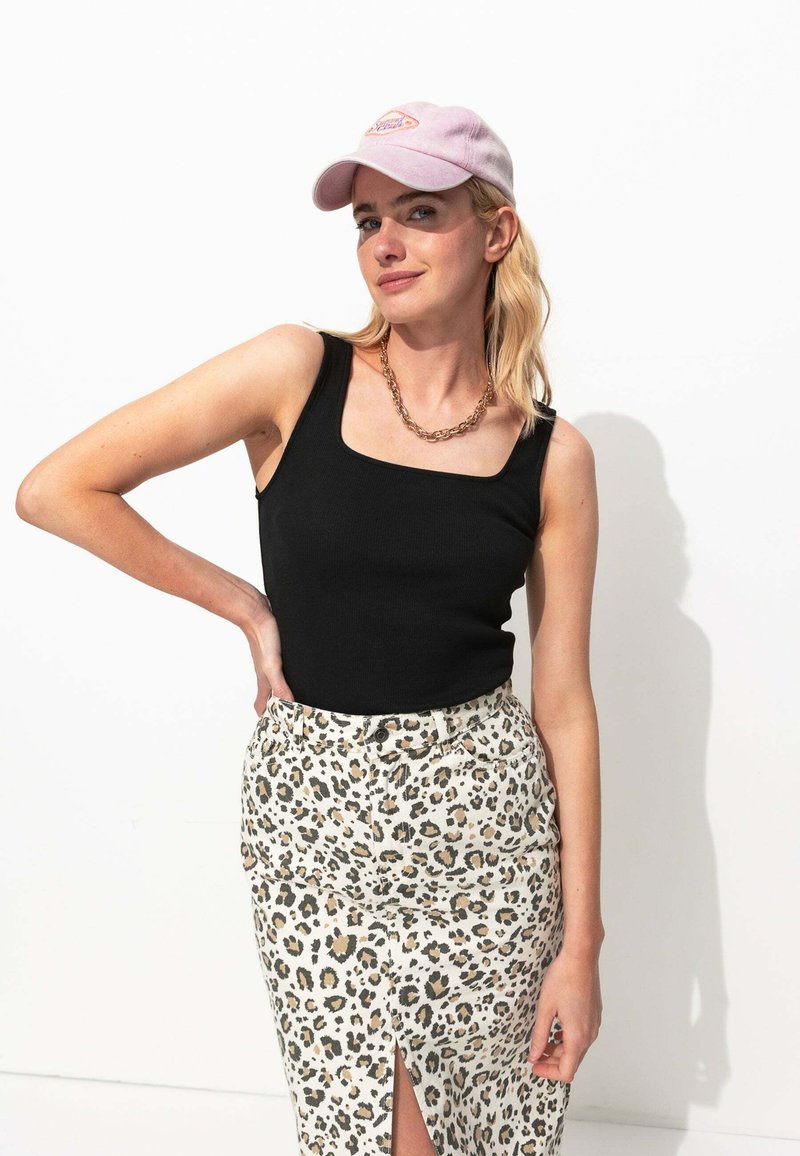 Débardeur noir à côtes porté avec une jupe léopard à fente haute. Une casquette de baseball rose pâle et un collier à chaîne épaisse complètent le look.