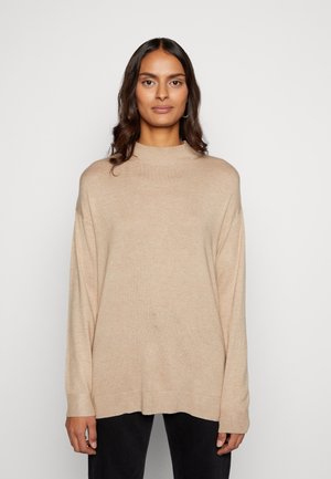 Suéter de punto acanalado beige con cuello alto y mangas largas, que presenta un corte relajado y un patrón texturizado. Sin cierres visibles.