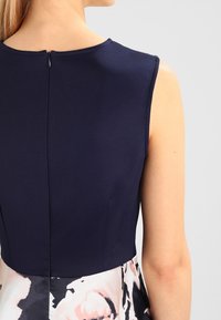 Námořnické bezrukávové šaty s přiléhavým vrškem a sukní s květinovým potiskem. Zapínání na zip vzadu; hladká textura.