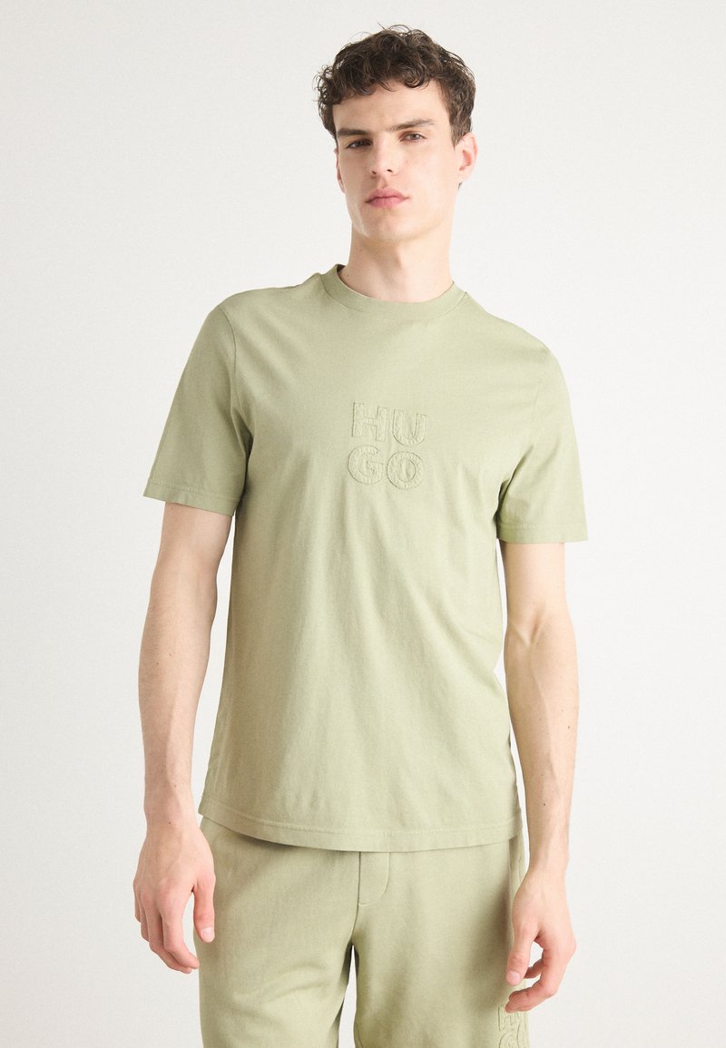 Light olive green T-shirt made of soft cotton. Features a round neckline and embroidered "HUGO" logo in the center. Short sleeves.