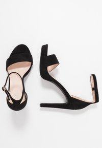 Svarta mocka högklackade sandaler med två breda remmar, öppen tå och en smal klack. Har en spänne för ankeln.