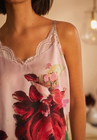 Helles rosa Satin-Camisole mit floralem Druck, der große rote und rosa Rosen zeigt, zarte Spitzenkante am Ausschnitt und dünne Träger.