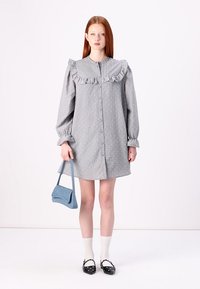 Abito grigio con bottoni, colletto arricciato, maniche lunghe e motivo a pois. Abbinato a una borsa blu, calze fino al ginocchio e scarpe con dettagli.