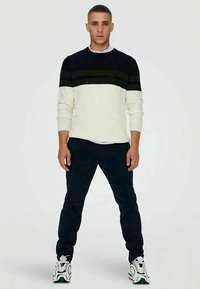 Sweater in navy, white, and green stripes; crew neck and long sleeves. Paired with dark pants and white sneakers with green accents.