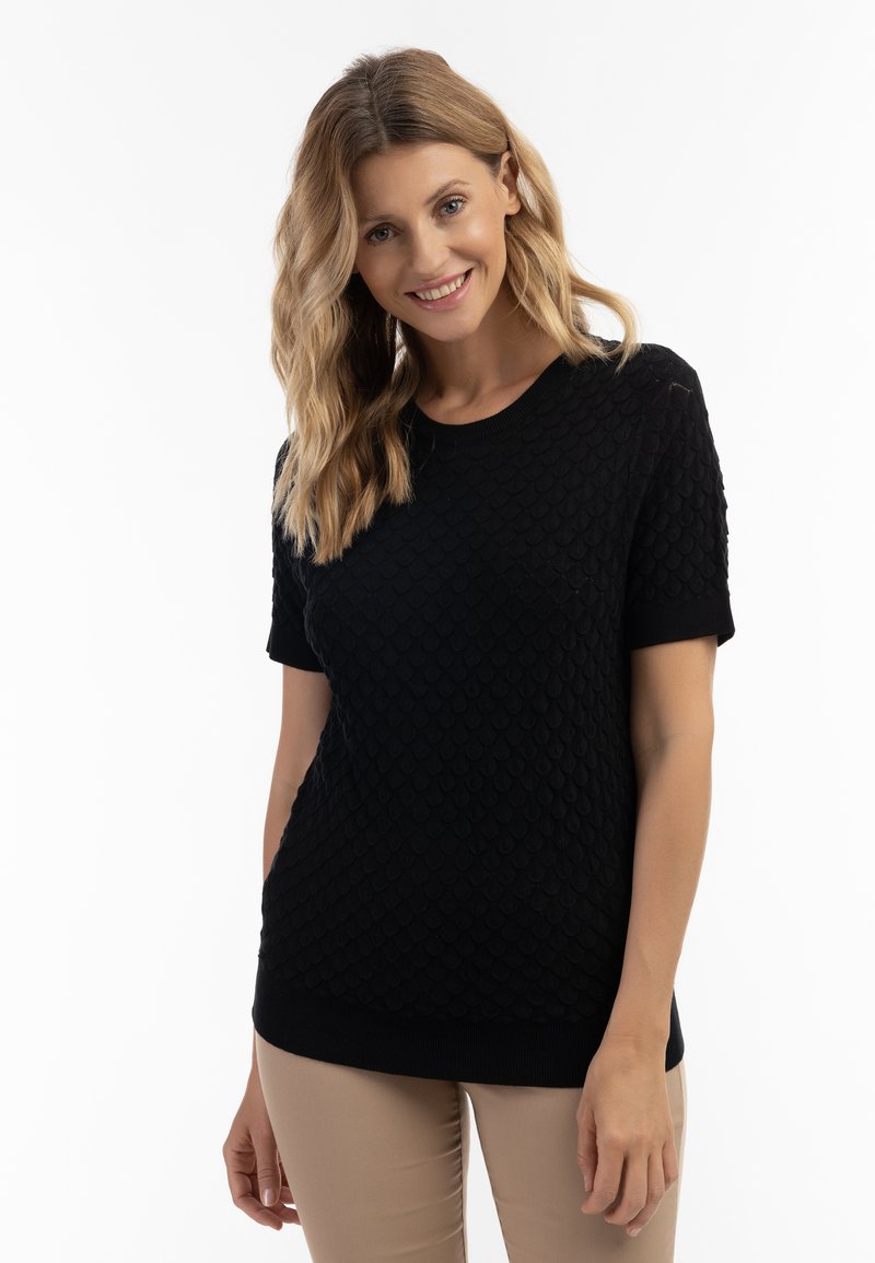 Sort strikket sweater med et struktureret diamantmønster, korte ærmer og rund hals. Båret med lyse beige, tætsiddende bukser.