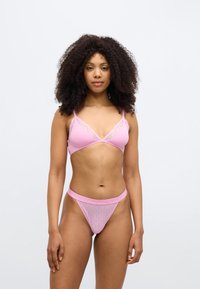 Ροζ μπραλέ με δαντελένιο τελείωμα και ρυθμιζόμενους ιμάντες, σε συνδυασμό με ταιριαστό διαφανές στρινγκ με γεωμετρικό σχέδιο και λογότυπο στη μέση.