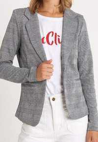 Šedé kostkované sako s přizpůsobeným střihem, vybavené strukturovanými rameny, výstřihem s výřezem a zapínáním na jeden knoflík.