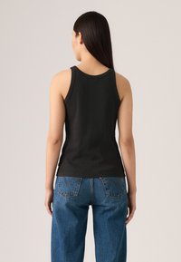 Svart ribbestrikket tanktopp med brede stropper, tettsittende fasong og rund utrigning. Sett sammen med blå høytalende denimjeans med baklommer.