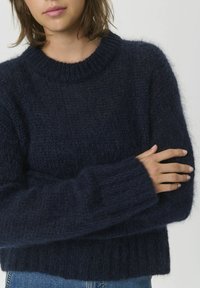 Navy blue knitted sweater with a round neckline, ribbed cuffs, and soft texture. Features loose-fitting sleeves and a relaxed silhouette.