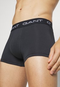 Boxeri din bumbac negri, cu un talie contrastantă neagră, pe care este inscripționat numele brandului "GANT" cu litere albe. Textură netedă, design ajustat.