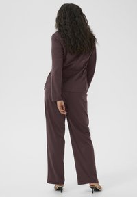 Veste de costume ajustée violette foncée à manches longues associée à un pantalon large assorti. Tissu texturé ; vue arrière avec cheveux ondulés.