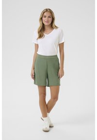 Olivgrön shorts med texturerad tyg, hög midja och sidofickor, i kombination med en enkel vit t-shirt med V-hals och avslappnade sneakers.