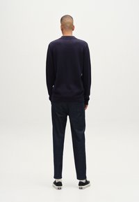 Marinblå stickad tr�öja med krage, i kombination med mörka jeans. Båda plaggen har en avslappnad passform, med subtila texturer och klassisk design.