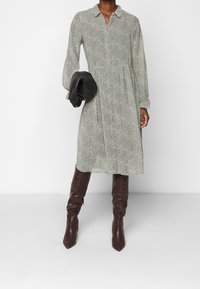 Largo vestido de botones con un patrón en espiga blanco y negro, que presenta un cuello y mangas largas, combinado con botas burdeos hasta la rodilla.