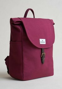 Burgundy kanvasryggsäck med klaffstängning, en läderrem med spänne, en framsideslogotyp och en sidoficka. Designad för avslappnad användning.