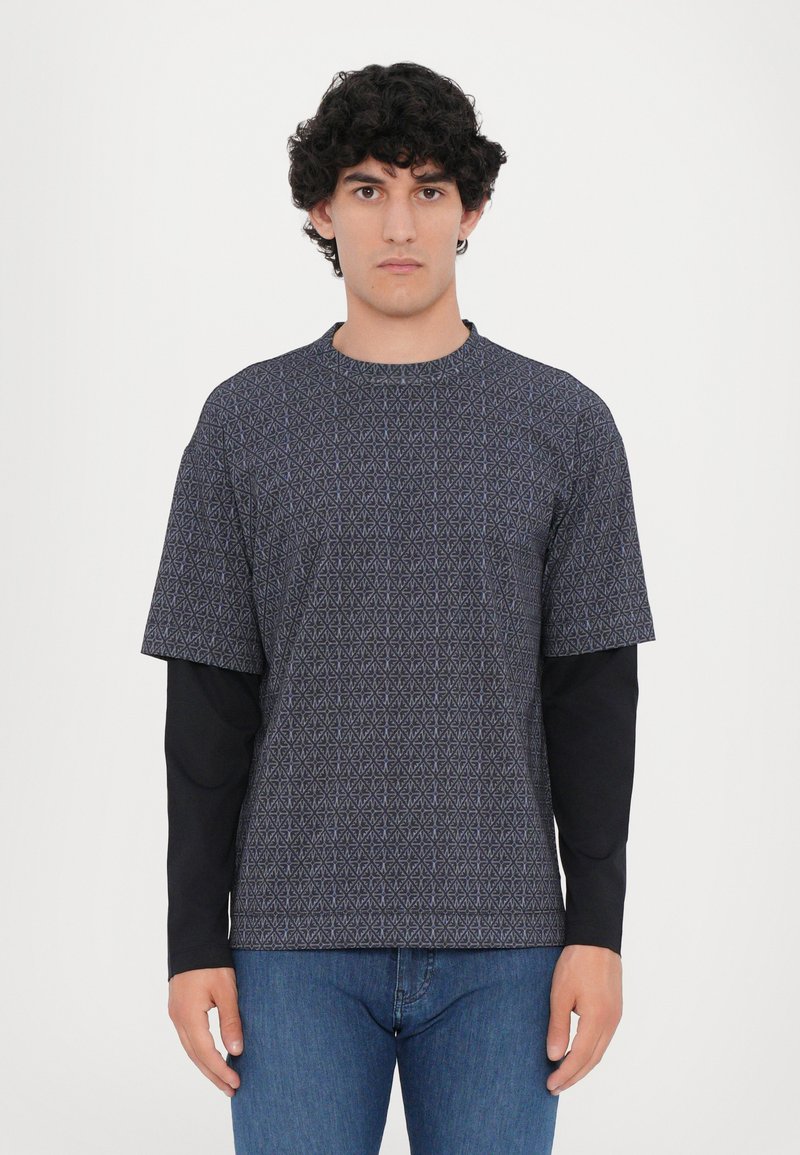 Kratkās piedurknes tumši zils T-krekls ar ģeometrisku rakstu, ar apaļu kakla izgriezumu un brīvu piegulumu, kārtots virs garām piedurknēm melnas bāzes kārtas.