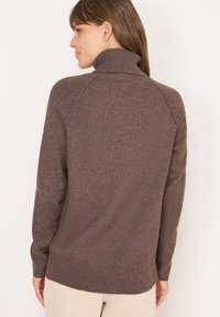 Pull en col roulé marron avec un tissu tricoté texturé, des poignets et un ourlet côtelés. Le design présente une coupe décontractée, idéale pour superposer.