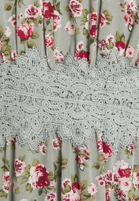 Robe fleurie en tissu gris décorée de roses rouges et roses, agrémentée d'une bordure en dentelle gris clair autour de la taille. Design texturé et plissé.