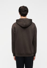 Sweat à capuche marron en tissu doux, avec une coupe décontractée, des poignets côtelés et une poche kangourou à l'avant.