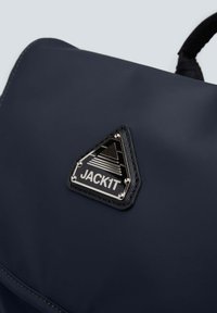 Zaino blu navy realizzato in tessuto resistente, caratterizzato da una toppa nera triangolare con accenti metallici e dettagli di cucitura.