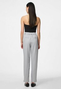 Pelēki pielāgoti bikses ar brīvu piegriezumu, elastīgu jostasvietu un diskrētām aizmugurējām kabatām. Modelis valkā melnu bezsoma topu un melnas kurpes.