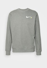 Grå sweatshirt i mjukt tyg, med rund halsringning, långa ärmar och en liten vit Nike-logga med ett gult hjärta på bröstet.