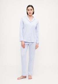 Ljusblå pyjamasset med långärmad knäppblus och löst sittande byxor, med detaljer på krage och manschetter. Mjuk, slät tyg.