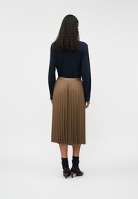 Fustă plisată maro cu un brâu orizontal, asortată cu o bluză albastră cu mânecă lungă. Pur tată cu ciorapi închiși la culoare și pantofi cu toc mic.