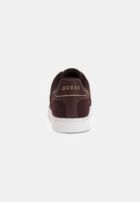 Brune ruskinds-sneakers med en maroon læderhæl. Har guld "GUESS" logo og hvid gummisko. Klassisk low-top design.