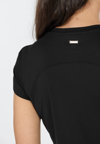 Schwarzes sportliches T-Shirt mit kurzen Ärmeln, das eine glatte Textur aufweist und ein kleines Markenetikett am hinteren Halsausschnitt hat.