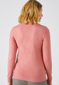 Pull rose à manches longues avec un ourlet et des poignets côtelés, texture lisse et coupe ajustée, montrant la vue arrière.