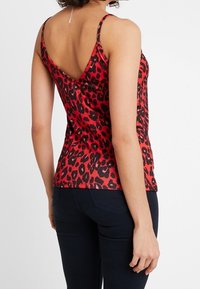 Röd satinaxelbandslinne med svart leopardmönster, med smala band och V-formad ryggdesign. Slät textur och åtsittande silhuett.
