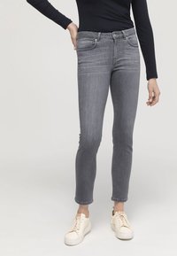 Grå stretchjeans med slim fit, featuring fem fickor, knäppning och subtila blekningar. Matchas med off-white sneakers.