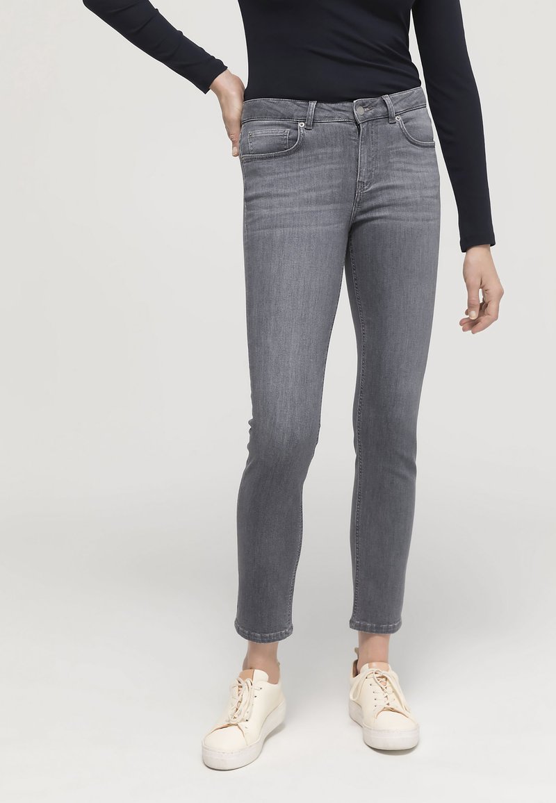 Grå stretchjeans med slim fit, featuring fem fickor, knäppning och subtila blekningar. Matchas med off-white sneakers.