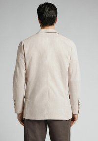 Blazer de lino beige con corte ajustado, solapas con muesca y cuatro botones en cada puño. Diseño sencillo con una textura suave.