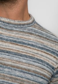 Pull en tricot avec un col rond côtelé, présentant un motif rayé bleu, beige et marron. Texture douce avec des détails de tricot visibles.