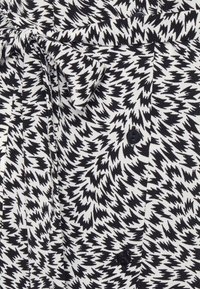 Mustavalkoinen kuviollinen kangaspaita, jossa on sahausmuotoinen malli, napitus edessä ja vyö vyötäröllä. Sujuva pinta.