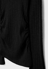 Černá žebrovaná pletenina s nařasením na bočním švu, vytvářející jemné záhyby a texturu.