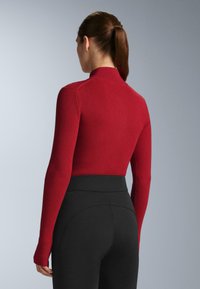 Röd ribbad polotröja med långa ärmar och figurnära design. Kombinerad med höga svarta leggings med en jämn och slät textur.