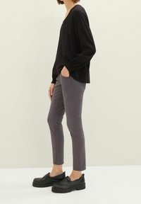 Top nero a maniche lunghe con scollatura a V, abbinato a pantaloni grigi slim-fit. Le calzature presentano scarpe nere slip-on con suola spessa.