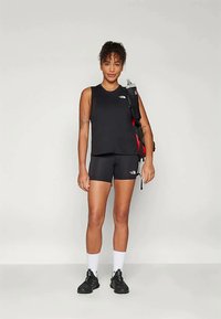 Juoda sportinė liemenė ir šortai su logotipu. Modelis dėvi juodus sportinius batus ir baltas kojines, laiko kuprinę su vandens buteliu.