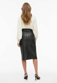 Mustat nahkainen midi-hame, jossa on istuva vyötärö, taka-taskut ja sileä pinta. Yhdistetty kevyen vaaleanbeigekraan blouseen.
