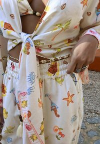 Lekki, kremowy strój składający się z bluzki z wiązaniem z przodu i spódnicy na elastycznej talii, ozdobiony kolorowymi morskimi i kwiatowymi wzorami.
